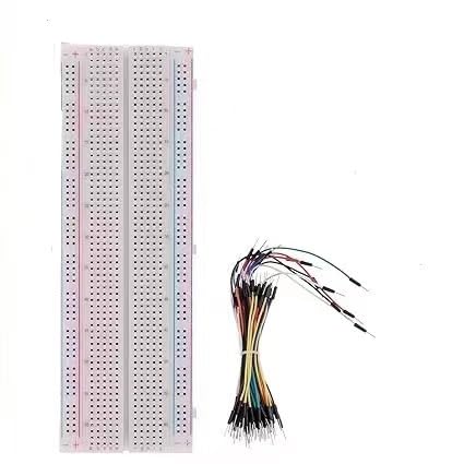 Protoboard blanca larga sin soldadura con líneas de riel rojas y azules en ambos bordes, junto a un manojo de cables puente flexibles